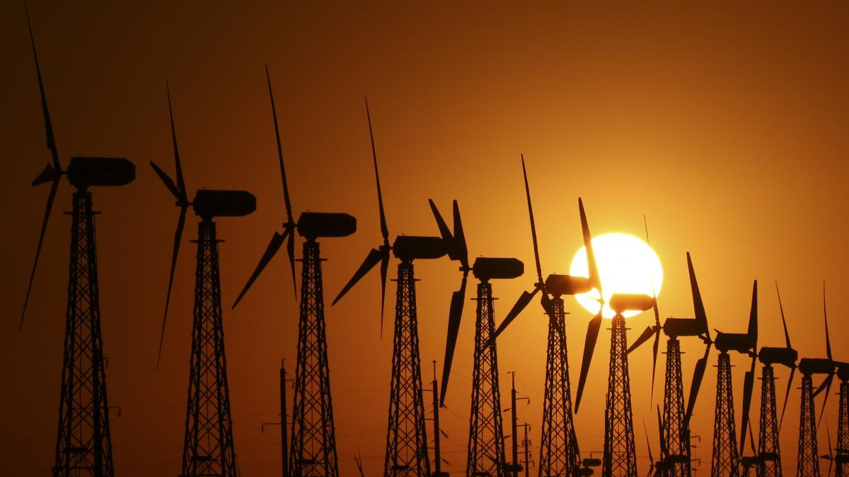 Row of wind turbines silhouetted against an orange sunset sky.