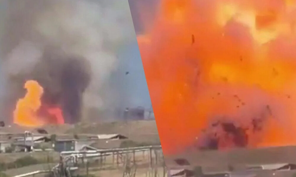 Industrial site on fire with large orange flames and thick black smoke rising from buildings.