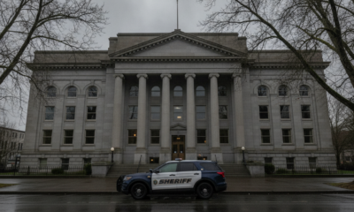 Gray neoclassical courthouse with tall columns and a sheriff SUV parked on the street in front on a cloudy day.