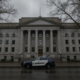 Gray neoclassical courthouse with tall columns and a sheriff SUV parked on the street in front on a cloudy day.
