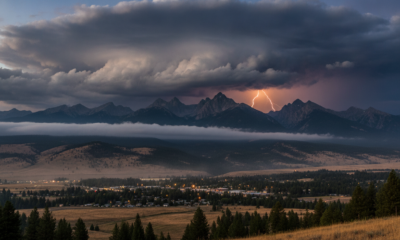 Stormy sky over jagged mountains with a bright lightning bolt striking near the peak; valley below with a small town and dark forest in foreground.